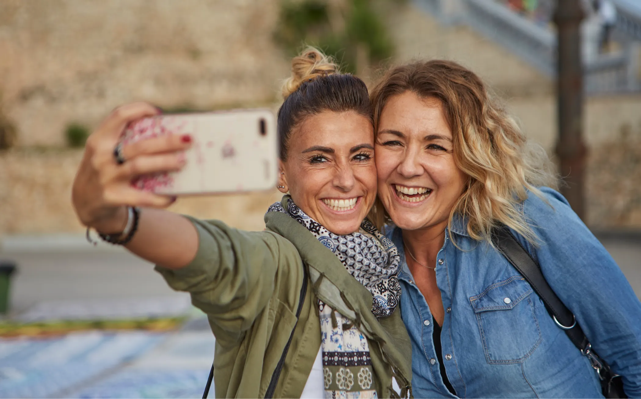 Dues amigues somrients fent-se un selfie juntes en un carrer exterior.