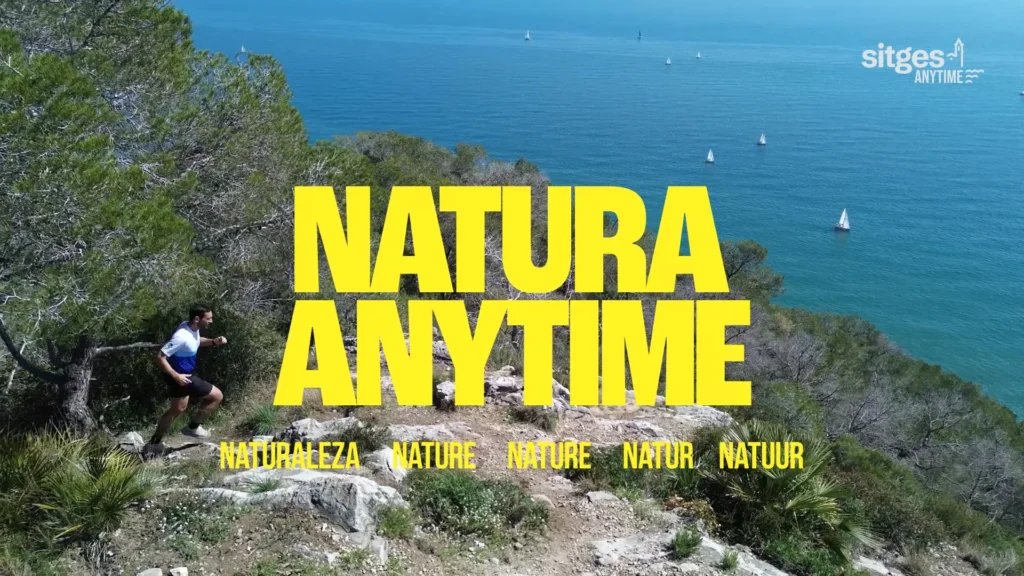 Corredor de montaña sobre un acantilado con vistas al mar y el texto 'NATURA ANYTIME' en amarillo.