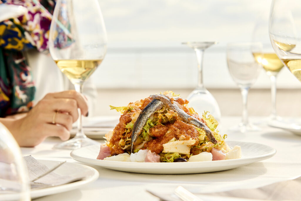 Plat de xató de Sitges amb una copa de vi blanc en un restaurant