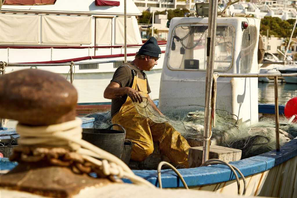 Pescador traient el peix de les xarxes a bord d’una embarcació al Port de Sitges-Aiguadolç