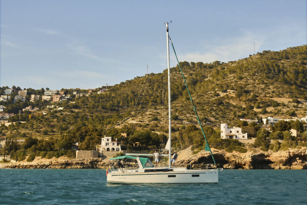 Veler navegant davant la costa de Sitges amb el paisatge del Garraf al fons