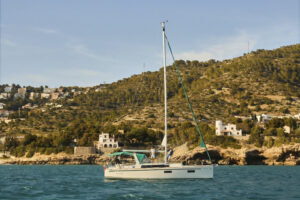 Veler navegant davant la costa de Sitges amb el paisatge del Garraf al fons