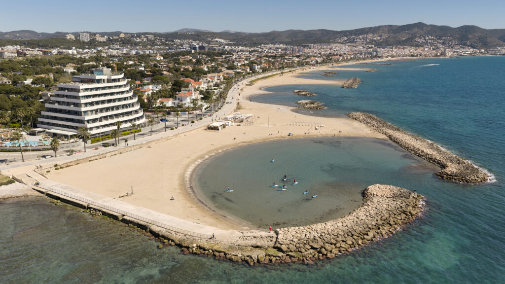 Vista aèria de les platges i el passeig marítim de Sitges amb el massís del Garraf al fons