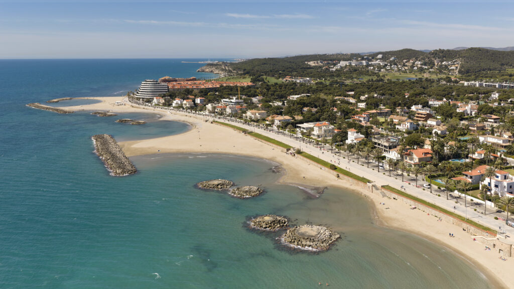 Vista aèria de les platges i el passeig marítim de Sitges, amb el litoral i les zones residencials al fons