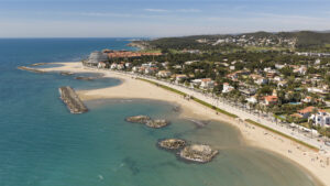 Vista aèria de les platges i el passeig marítim de Sitges, amb el litoral i les zones residencials al fons