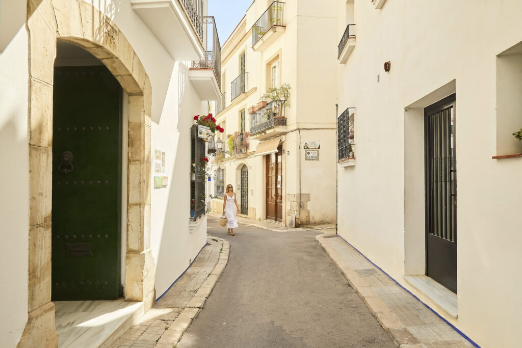 Dona passejant per un carrer estret del nucli antic de Sitges, entre façanes blanques