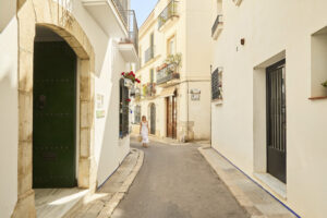 Dona passejant per un carrer estret del nucli antic de Sitges, entre façanes blanques